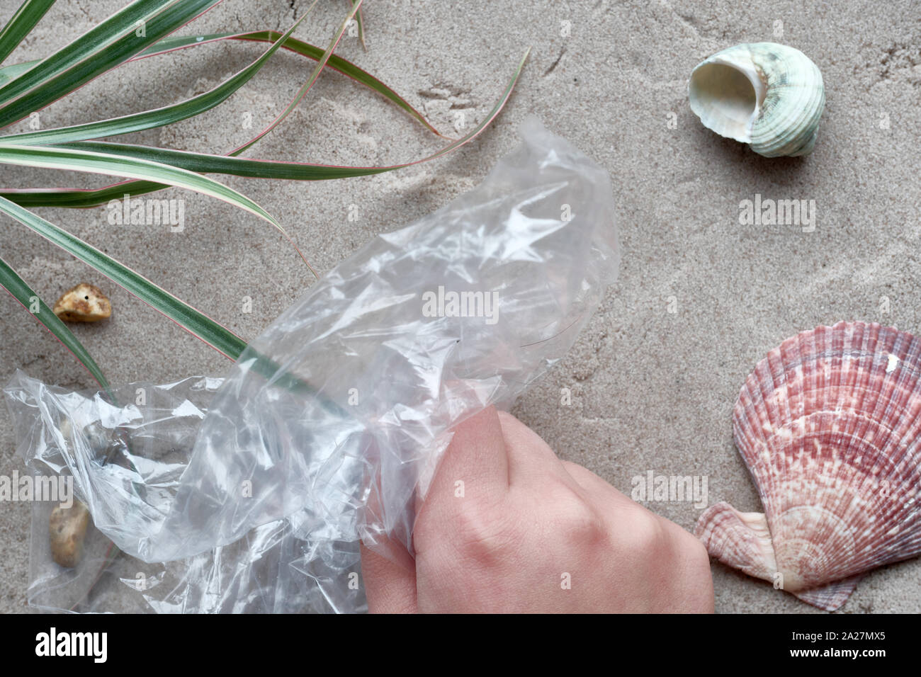 Bambino la mano il prelievo di plastica dalla spiaggia sabbiosa. Inquinamento di plastica è nocivo per la vita marina. Concetto ambientale contro uso singola in plastica. Foto Stock