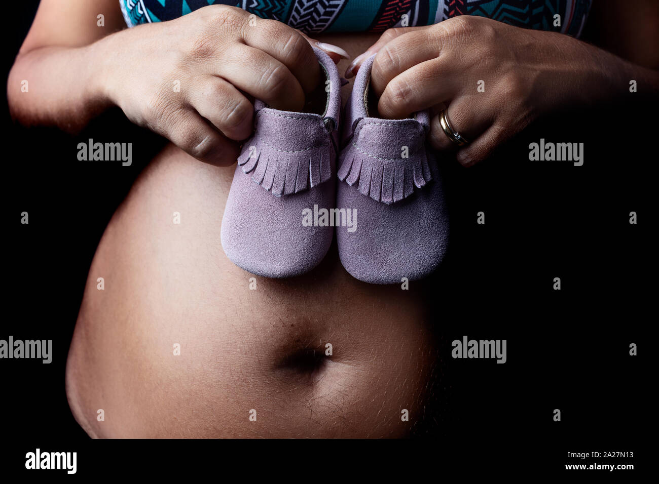 Dettaglio della donna incinta azienda scarpe per bambini contro il suo ventre. Foto Stock