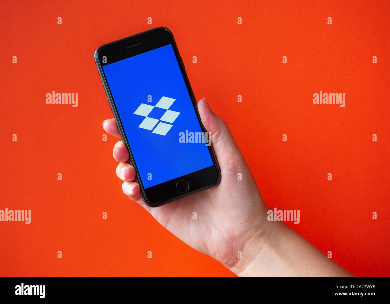Kiev, Ucraina - 1 Ottobre 2019: Studio colpo di mano azienda Apple iPhone 8 con Dropbox logotipo sulla schermata. Isolato su uno sfondo arancione. Foto Stock
