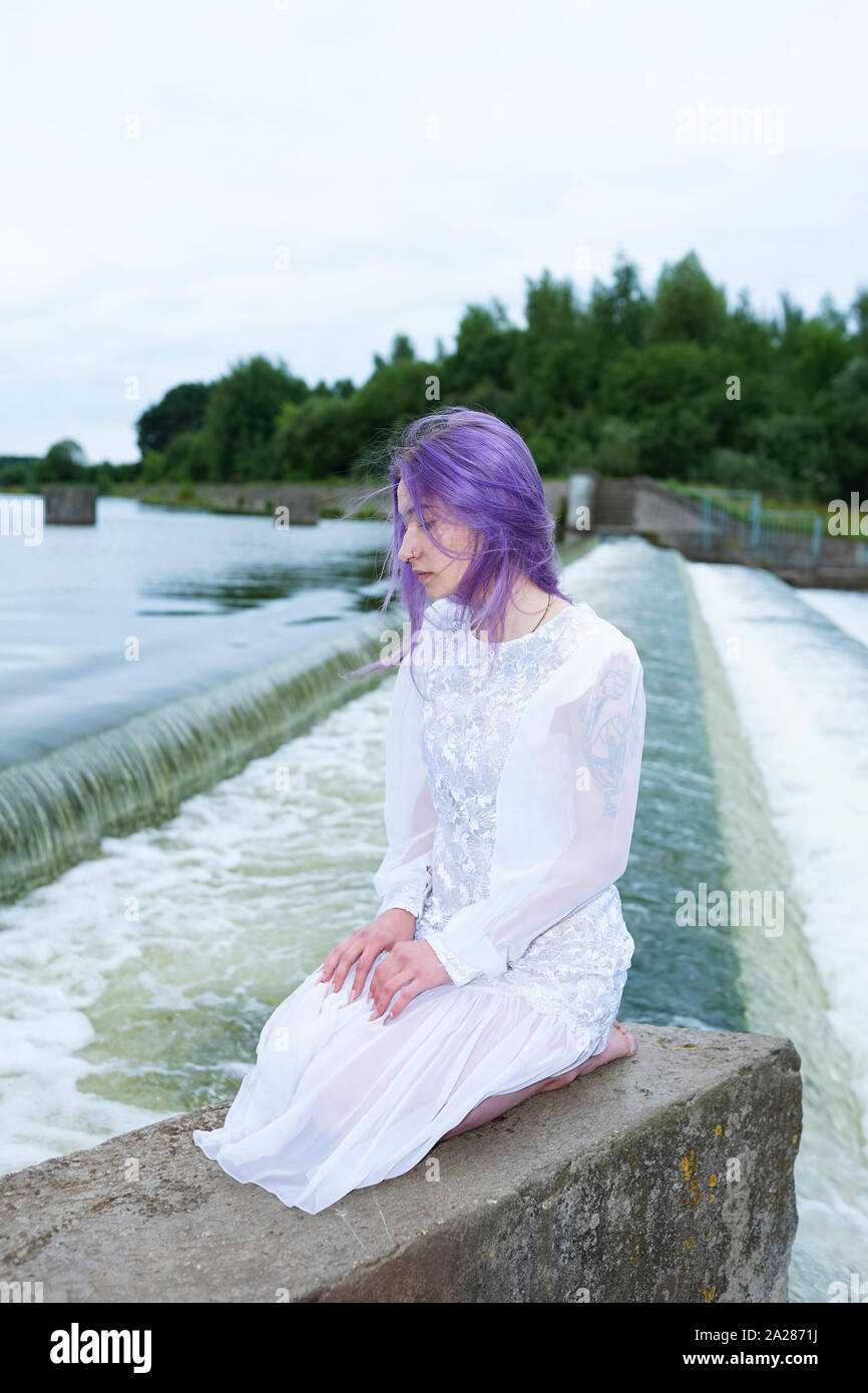 Donna seduta sulle ginocchia e nei pressi di una cascata Foto Stock