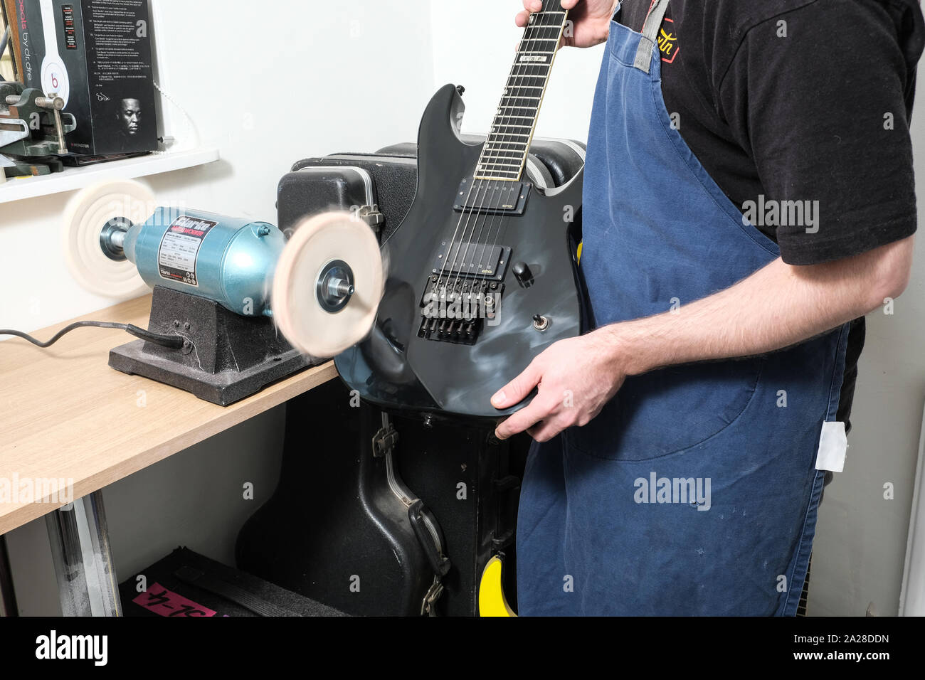 Un tecnico di chitarra o tech nella sua bottega utilizzando una macchina di lucidatura per lucidare il corpo di una stratocaster chitarra elettrica Foto Stock
