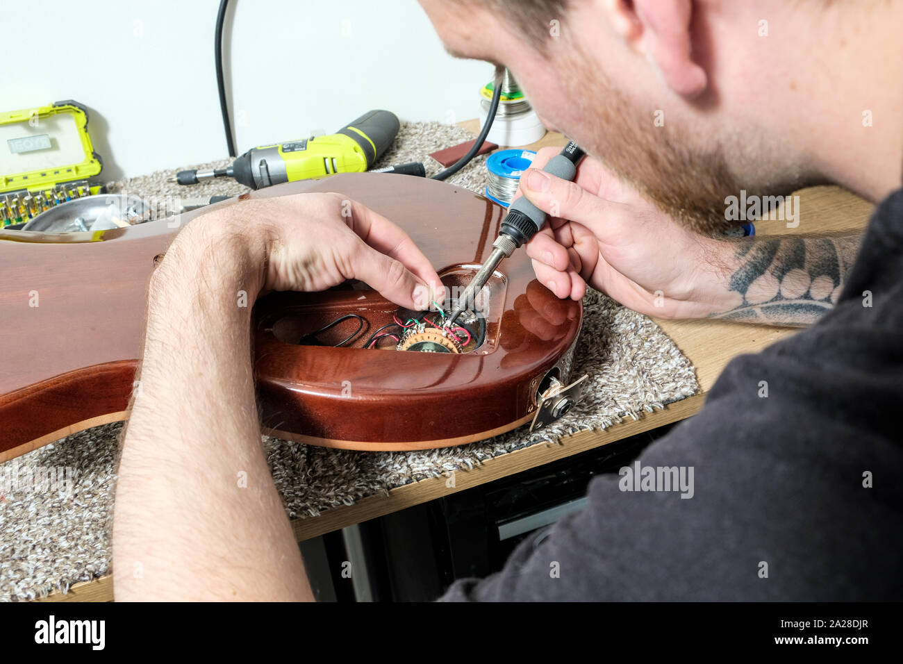 Un tecnico di chitarra o tech, nella sua bottega, la saldatura di una riparazione entro il corpo di una chitarra elettrica. Foto Stock