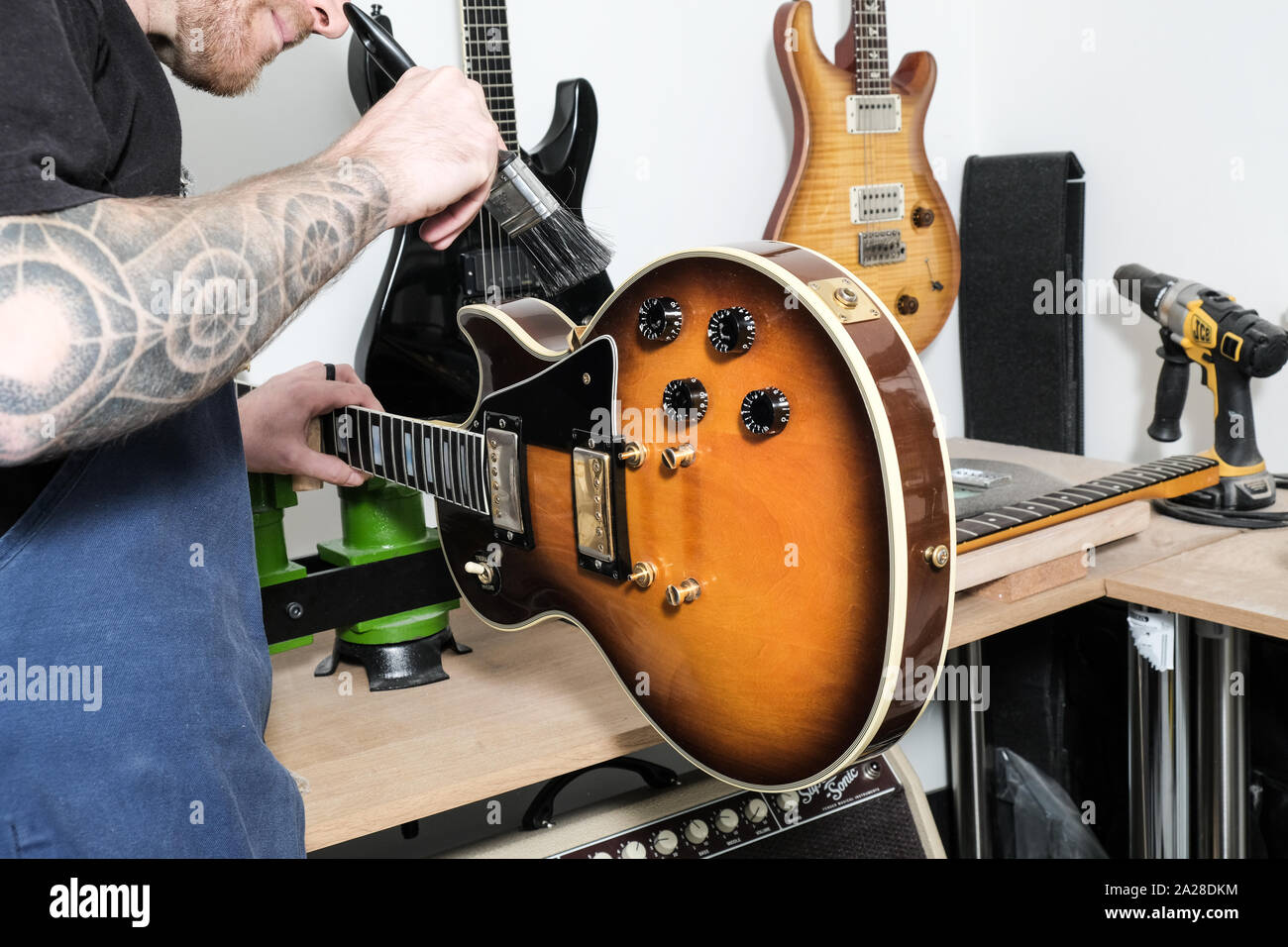 Un tecnico di chitarra, o tech, pulizia del corpo di una Gibson Guitar con un pennello. La chitarra è stretto in una morsa Foto Stock