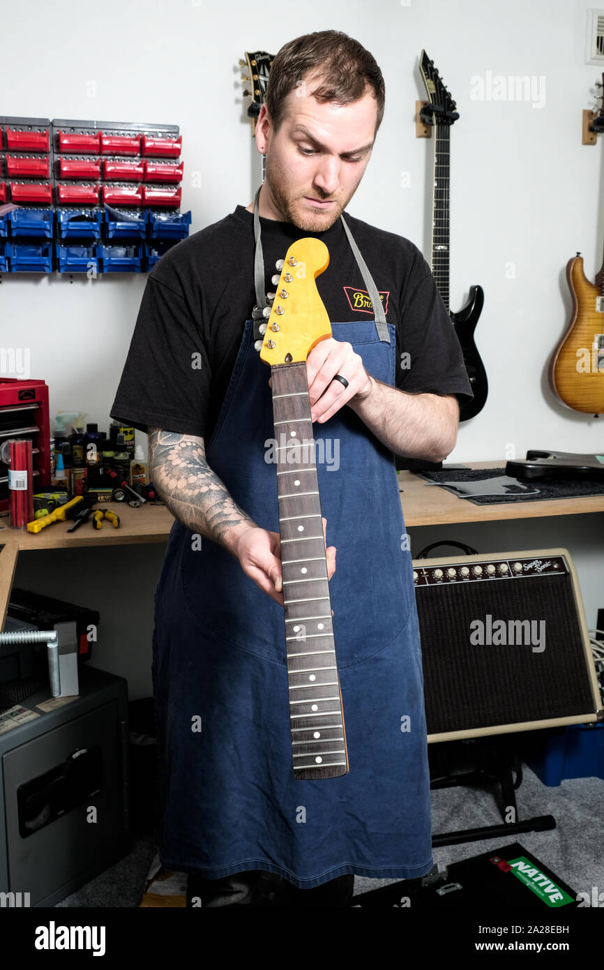 Una chitarra tecnico che lavora su un collo di una stratocaster chitarra. In questo quadro che egli è nel suo laboratorio e verifica che il fret board è diritta Foto Stock