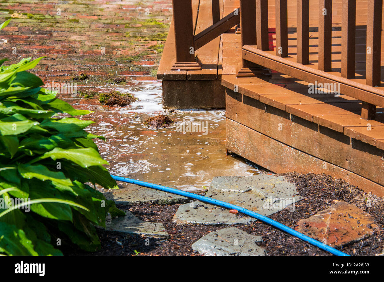 Pozza d'acqua marrone con schiuma di sapone su un patio di mattoni vicino a  un marrone a ponte di legno. Vi è acqua proveniente dal ponte Foto stock -  Alamy