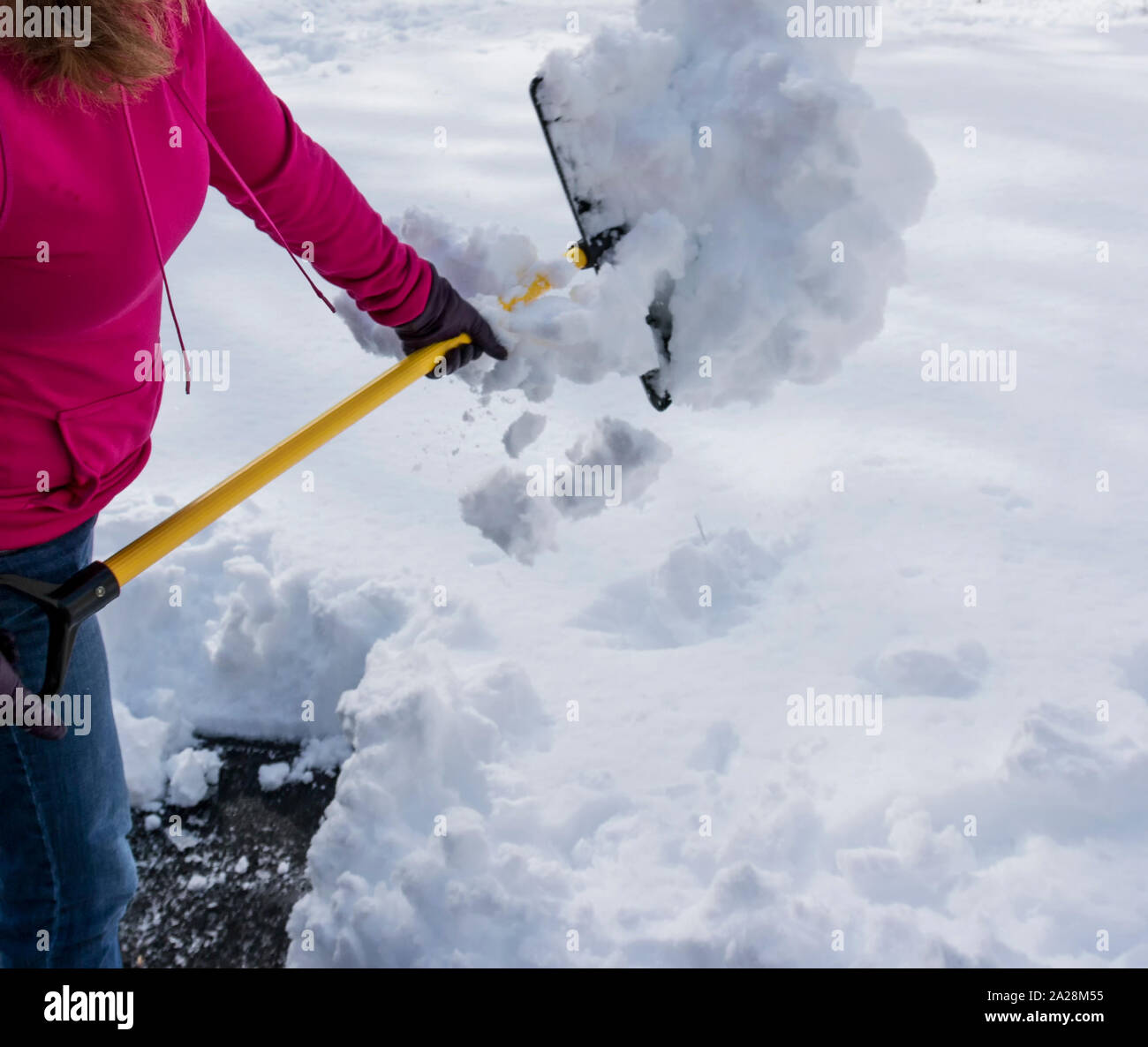 Una donna è spalare su un piede di neve indossando un rosa felpa con cappuccio e guanti neri dopo una molla tempesta di neve nel Long Island, New Yotk. Foto Stock