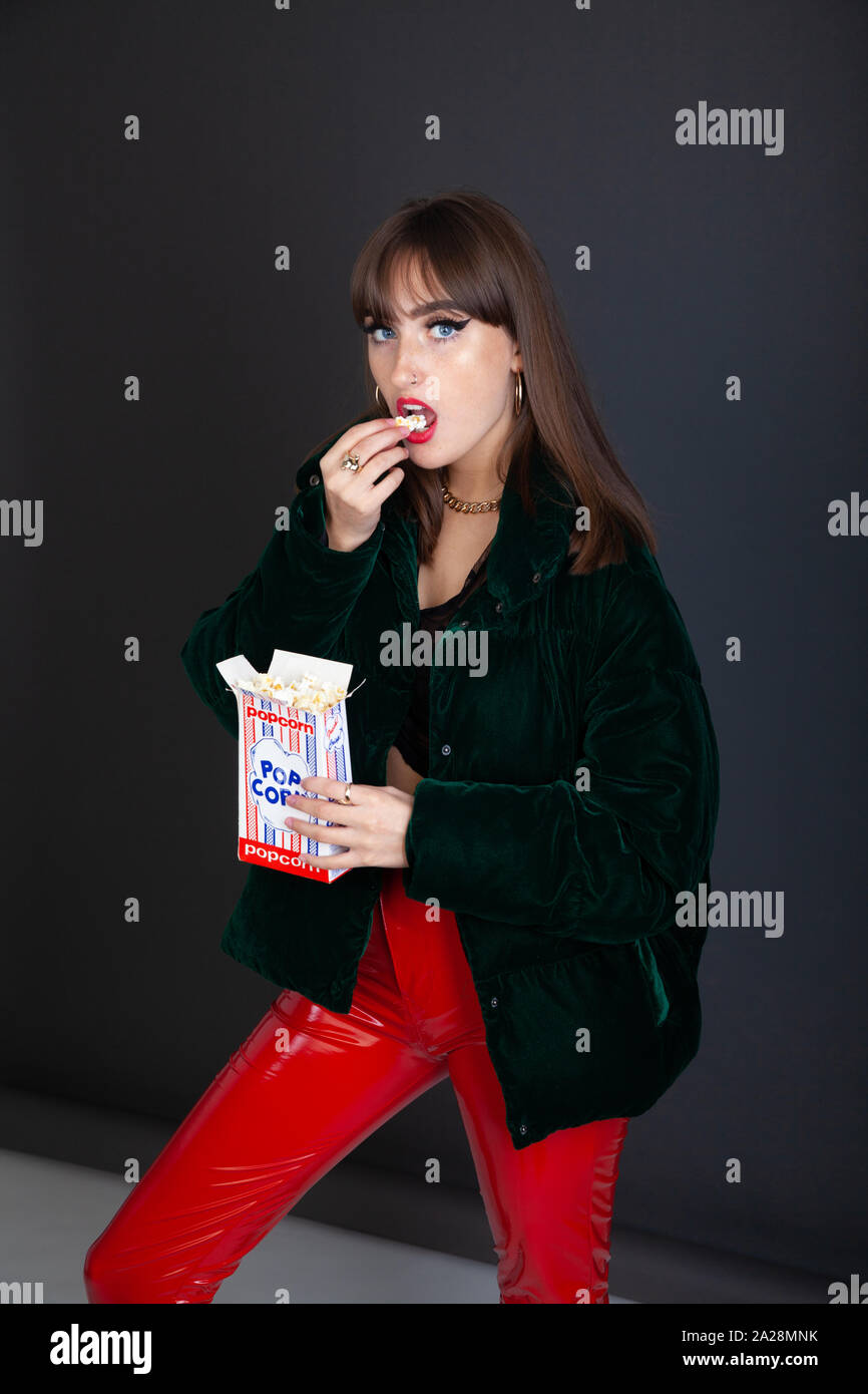 Una moda giovane donna indossa rosso brillante pantaloni in PVC e mangiare pop corn. Foto Stock