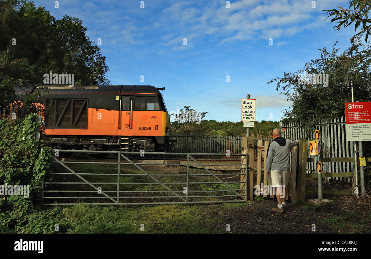 Un arancione locomotiva diesel attraversa Mares vicino passaggio a livello come un viandante attende il passaggio sulla linea ferroviaria linea di diramazione di Lynemouth power station. Foto Stock