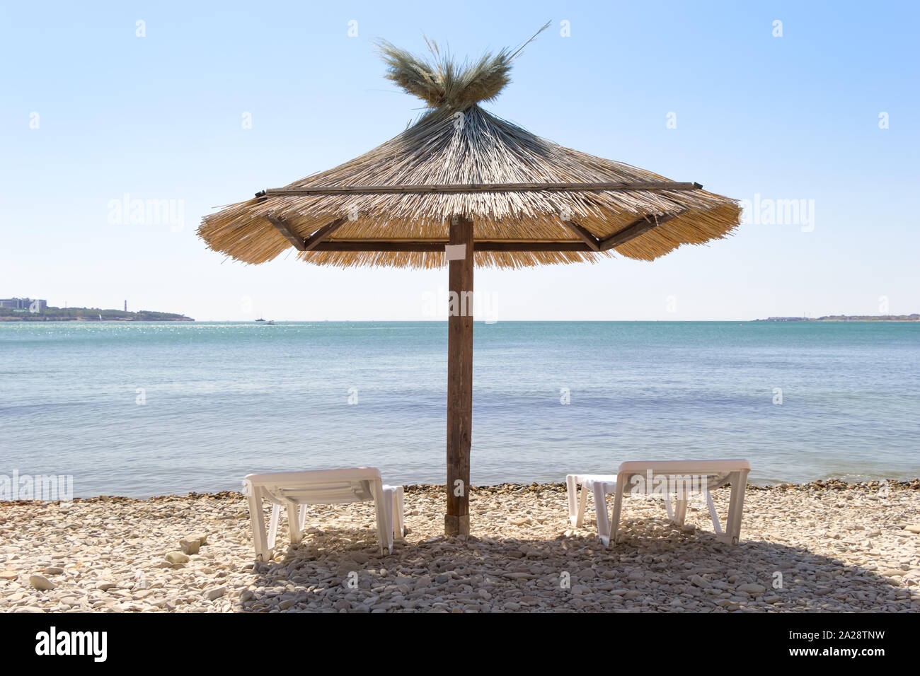 Sfondo di vacanza. Grande ombrello in un centro e due sedie a sdraio sulla spiaggia. Vista da dietro. Giornata di sole. Foto Stock