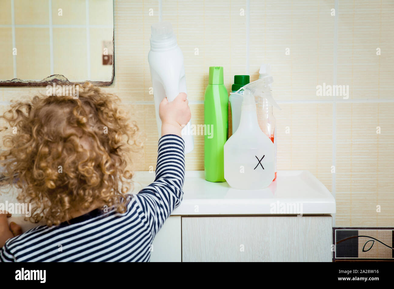 Bambino raggiunge prodotti chimici di uso domestico. Tenere lontano dalla portata dei bambini. Pericoli a casa per i bambini del concetto. Foto Stock