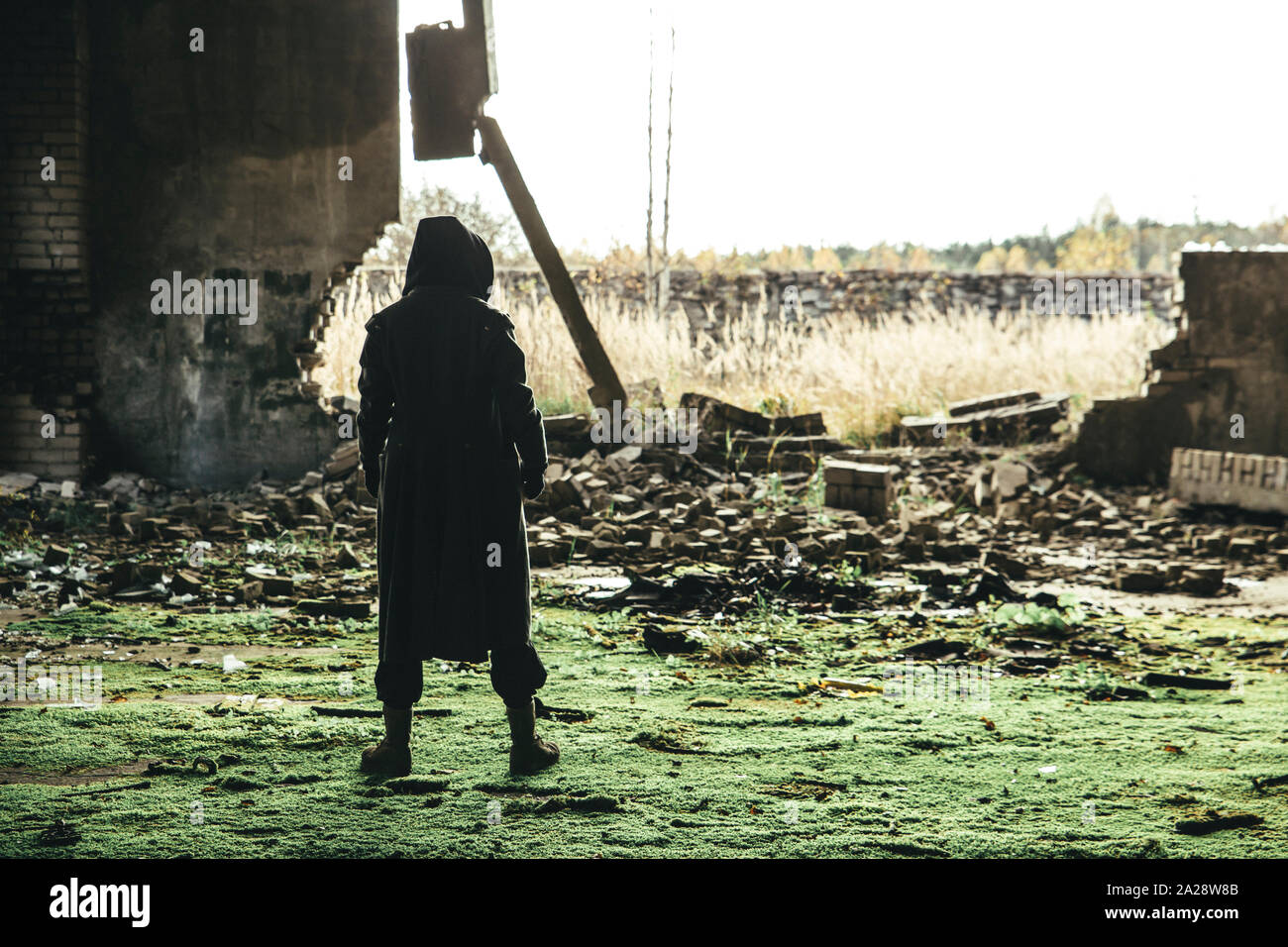 Grave uomo incappucciato indossando rivestire in piedi in rovine post-apocalittico. Foto Stock