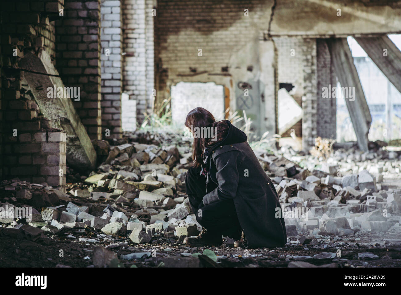Triste uomo si inginocchia e guarda alle rovine post apocalisse sulla terra, mattoni caduti sullo sfondo. Foto Stock