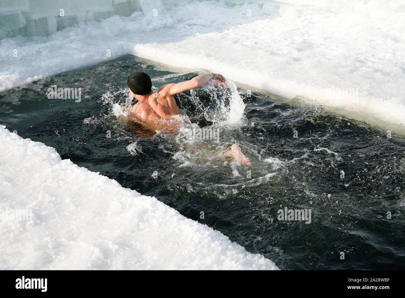 L uomo è il nuoto all'esterno nel foro di ghiaccio nel lago d'inverno. L'uomo dippes in un foro di ghiaccio. Foto Stock