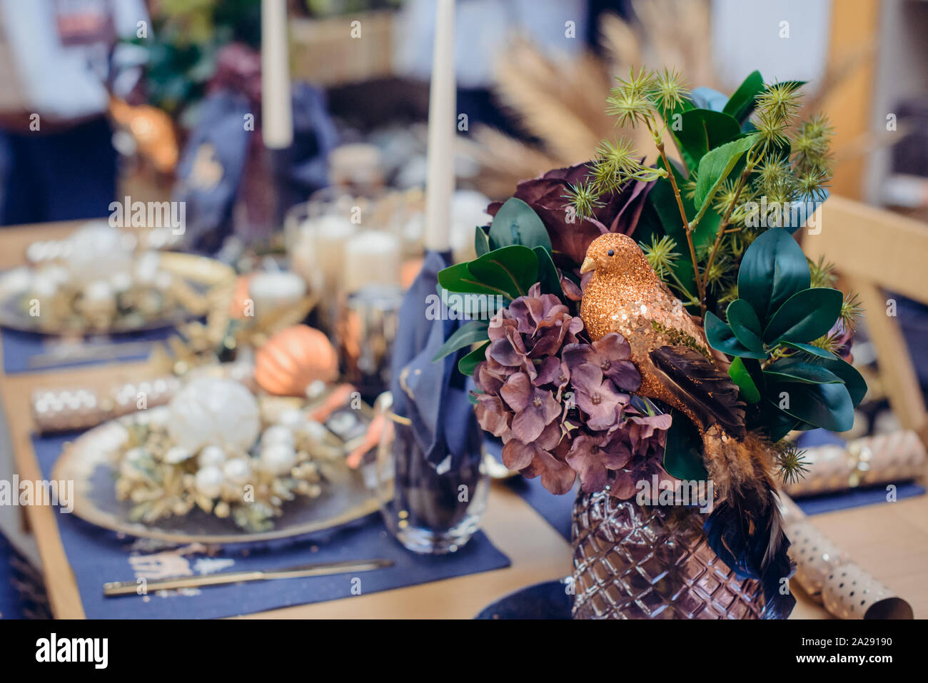 Esotico bouquet di natale decorazione con shiny bird su christmastime impostazione tabella, pappa di festa con graziosi dettagli e candele in blu e gol Foto Stock