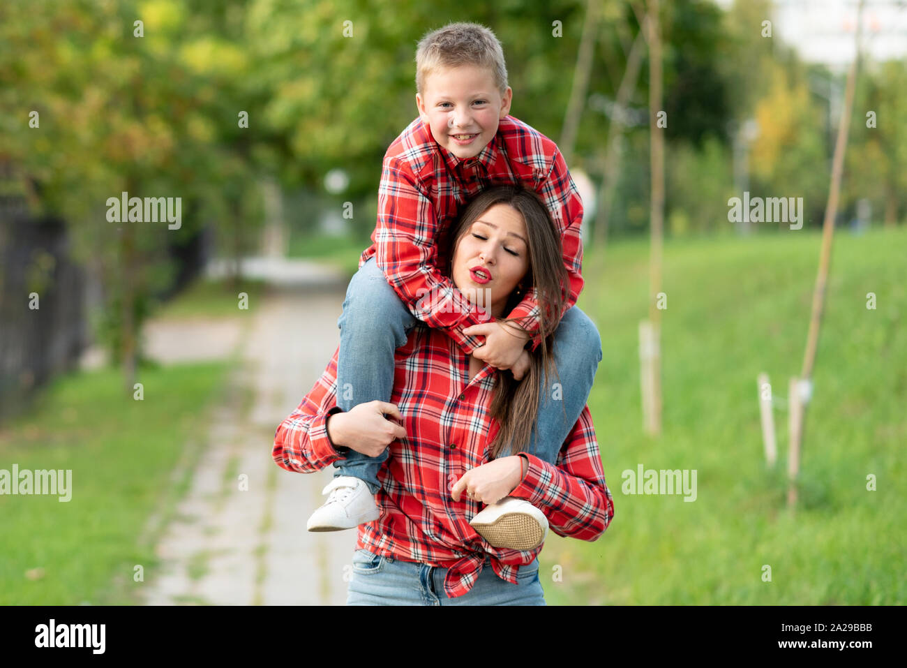 La mamma con un tormentato espressione sul viso, porta un figlio sorridente sulle sue spalle. Foto Stock