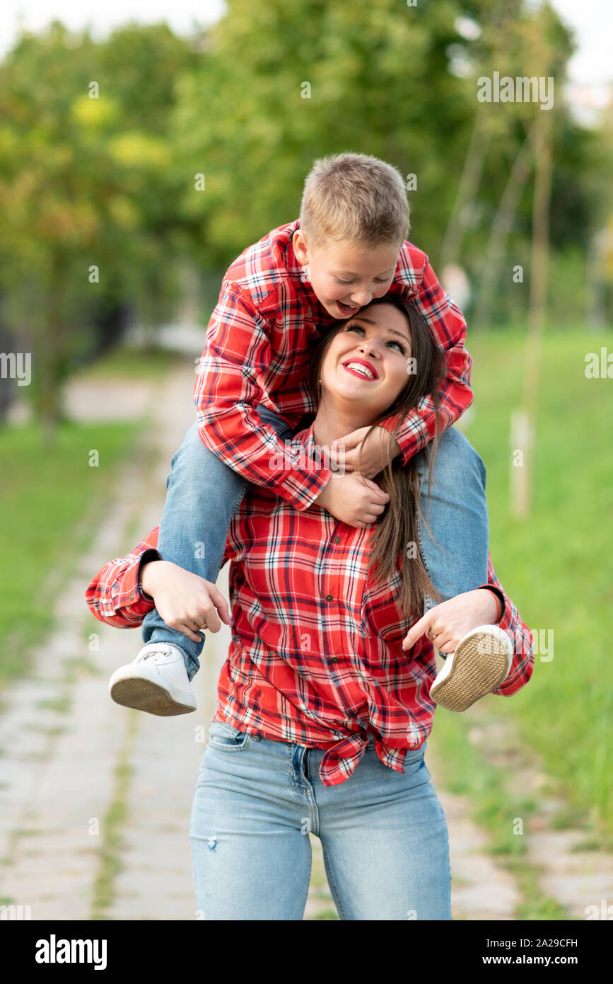 Mom, sorridente, porta un figlio sulle sue spalle. Foto Stock