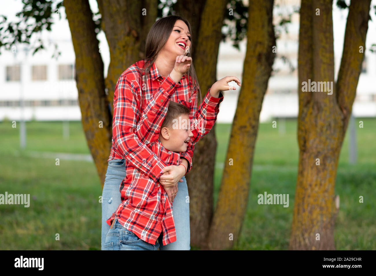 Mom, ridevano allegramente, abbraccia il suo figlio, che squinted e ha sollevato le sue mani verso l'alto. Foto Stock