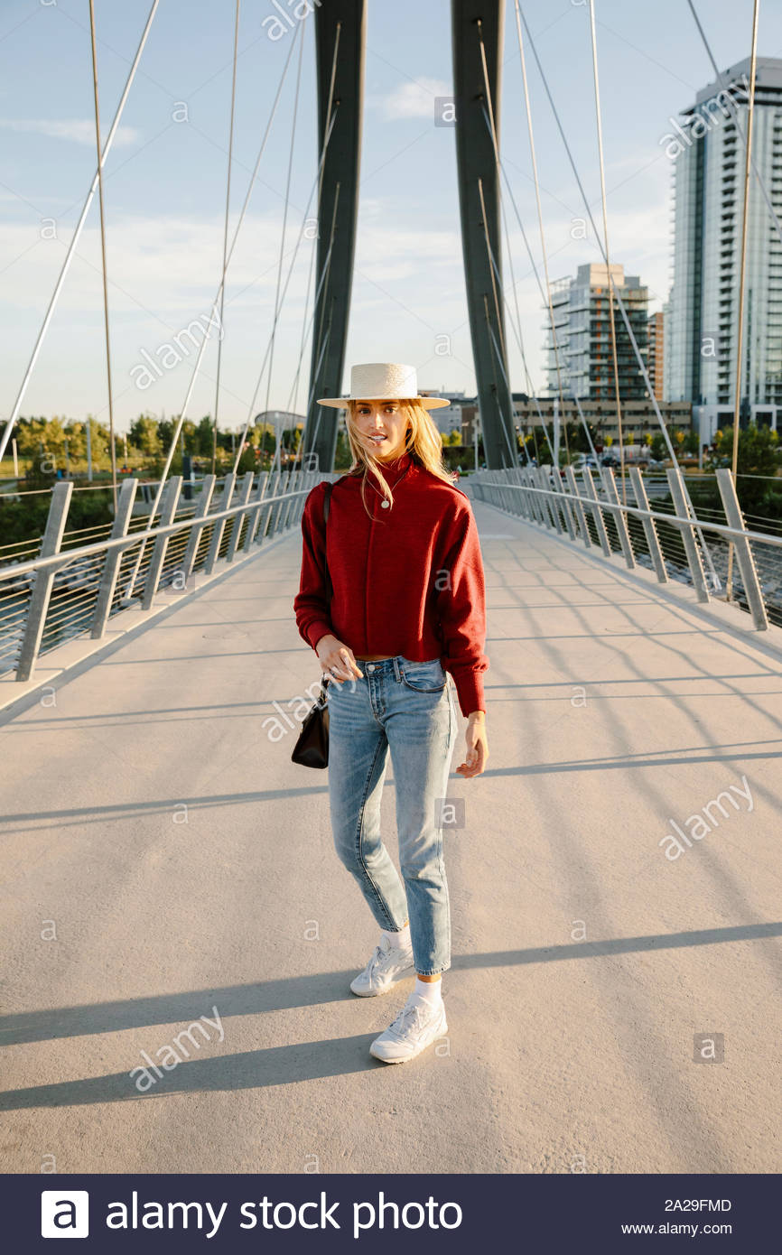 Ritratto fiducioso giovane donna in hat sul soleggiato, ponte urbano Foto Stock