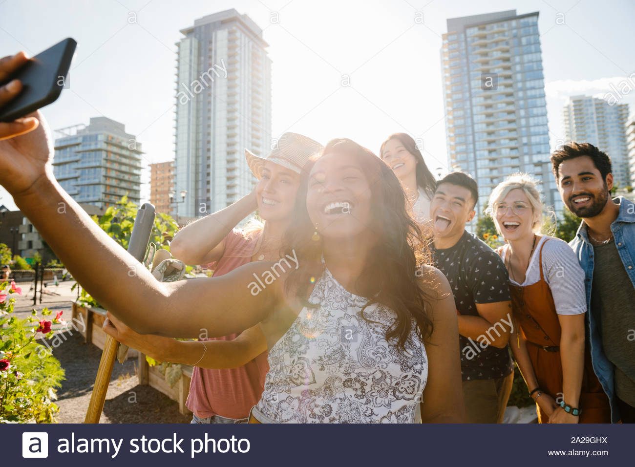Felice, giocoso giovani amici adulti tenendo selfie con la fotocamera del telefono nella soleggiata, urban comunità giardino Foto Stock