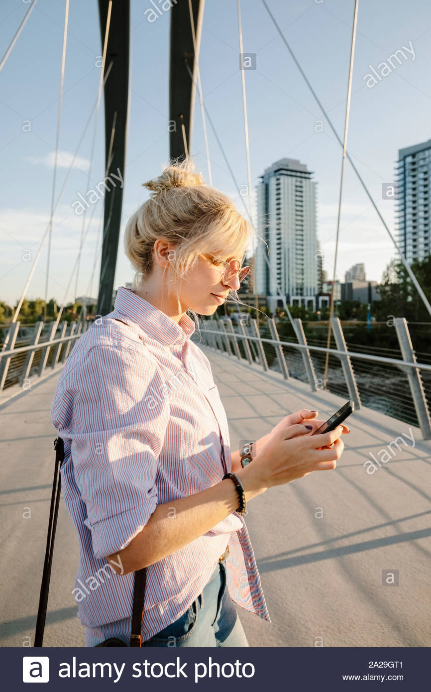 Giovane donna utilizzando smart phone sul soleggiato, ponte urbano Foto Stock