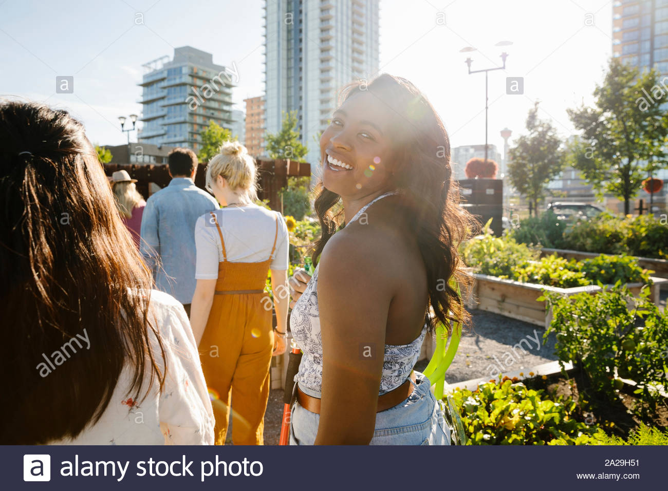 Ritratto felice e spensierato giovane donna con gli amici nella soleggiata, urban comunità giardino Foto Stock