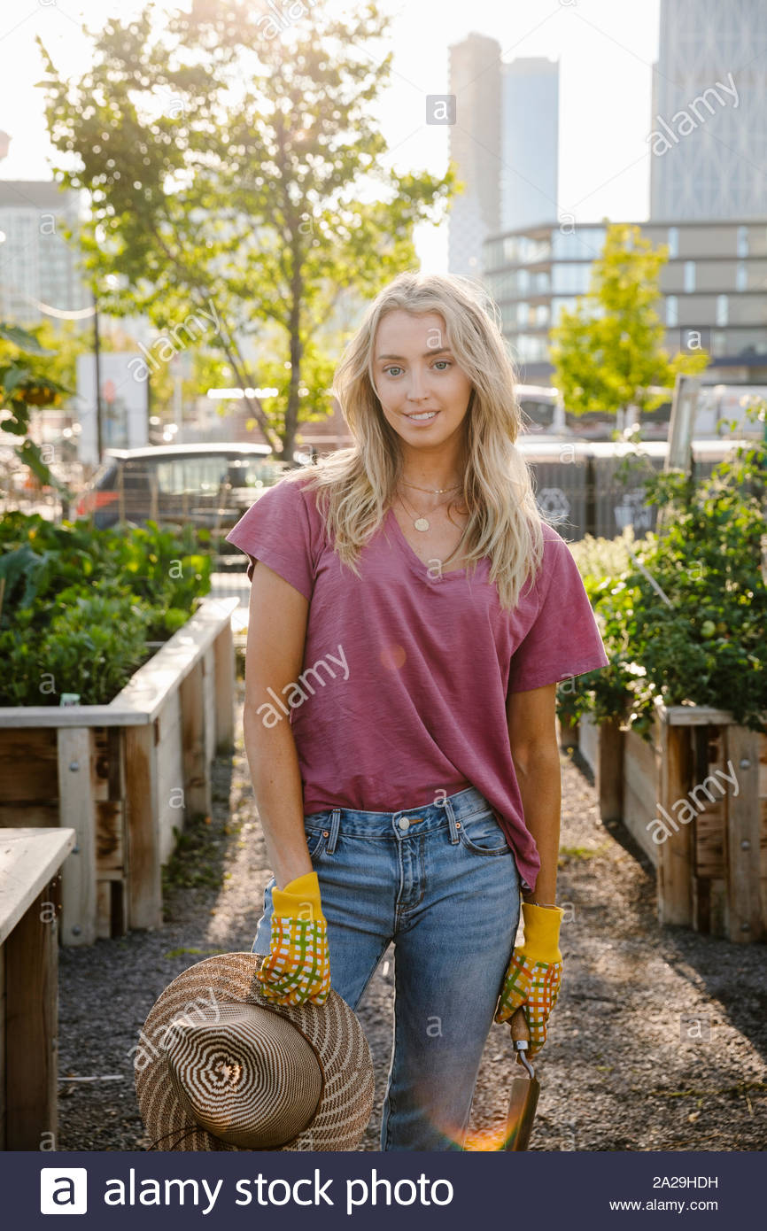 Ritratto fiducioso giovane donna nella soleggiata, urban comunità giardino Foto Stock