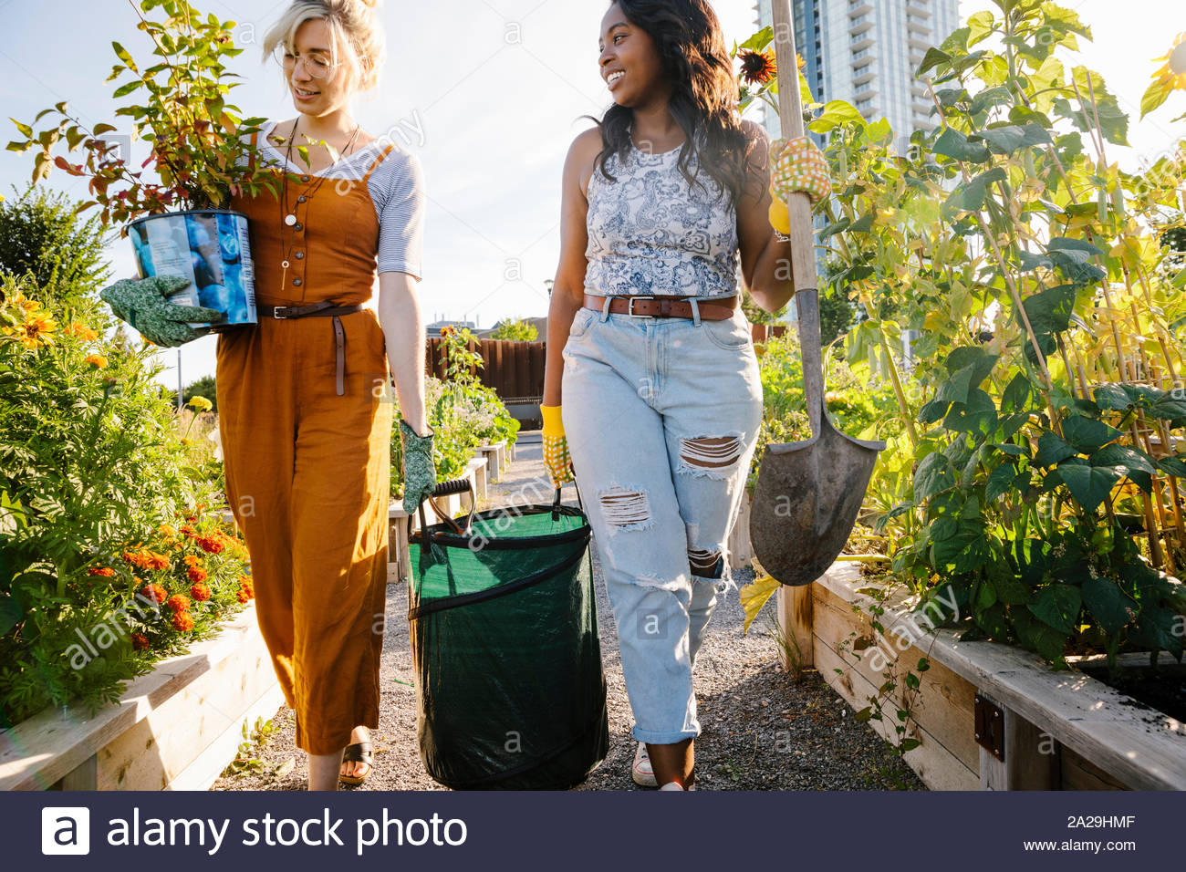 Le giovani donne che trasportano attrezzatura nel soleggiato, comunità urbana garden Foto Stock