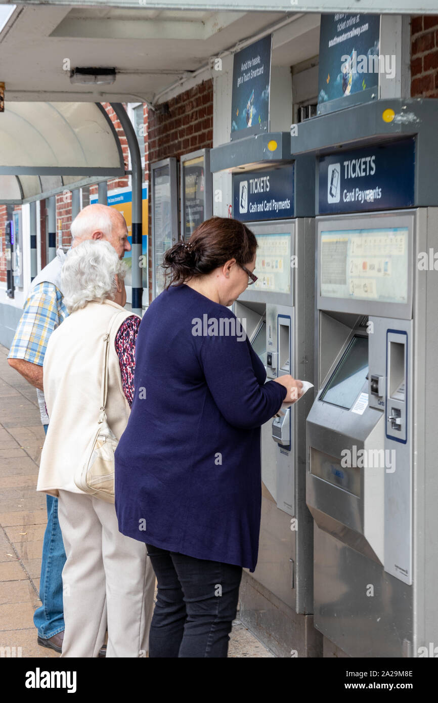 Una donna di mezza età e una coppia di anziani acquistando i biglietti del treno da una stazione ferroviaria ticket machine Foto Stock