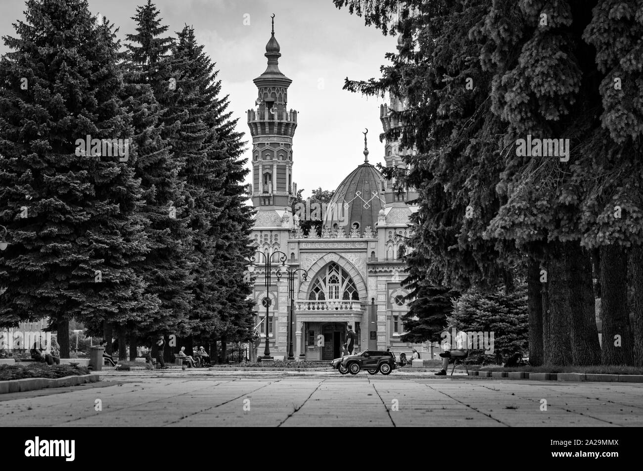 Vladikavkaz, Russia - 07 18 2019: Persone aventi il resto sulla piazza tra splendidi pini secolari di fronte sunnita moschea Mukhtarov Foto Stock