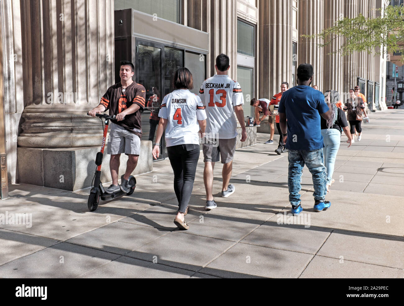 A Cleveland Browns tifoso rides uno scooter su un marciapiede in downtown Cleveland, Ohio, USA mentre altri tifosi a piedi da prima del gioco. Foto Stock