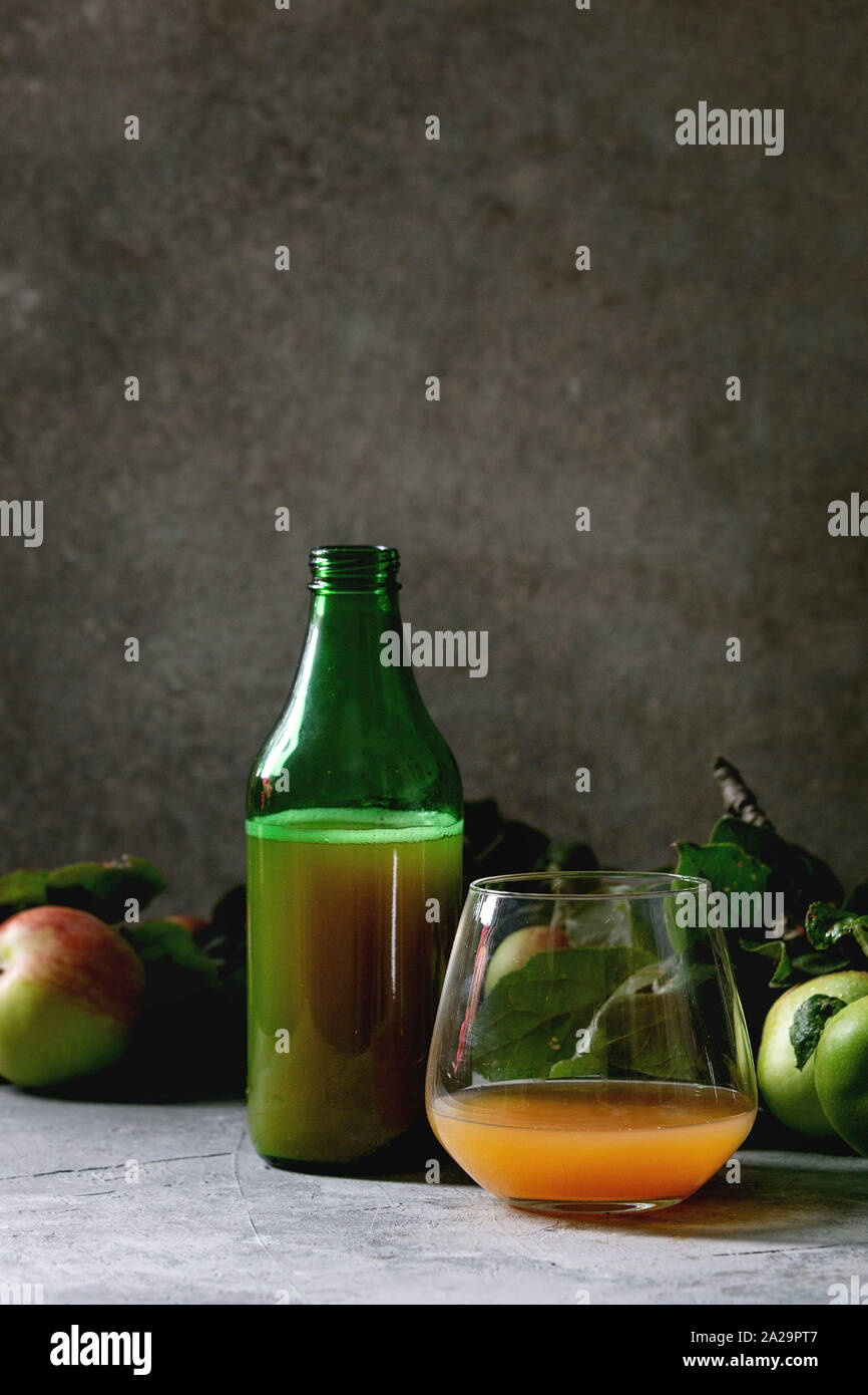 Bottiglie di vetro ang di sidro di mela a basso tenore di alcol bere con giardino di mele con foglie e rami sulla tavola con sfondo scuro. Autunno home la mietitura. Foto Stock