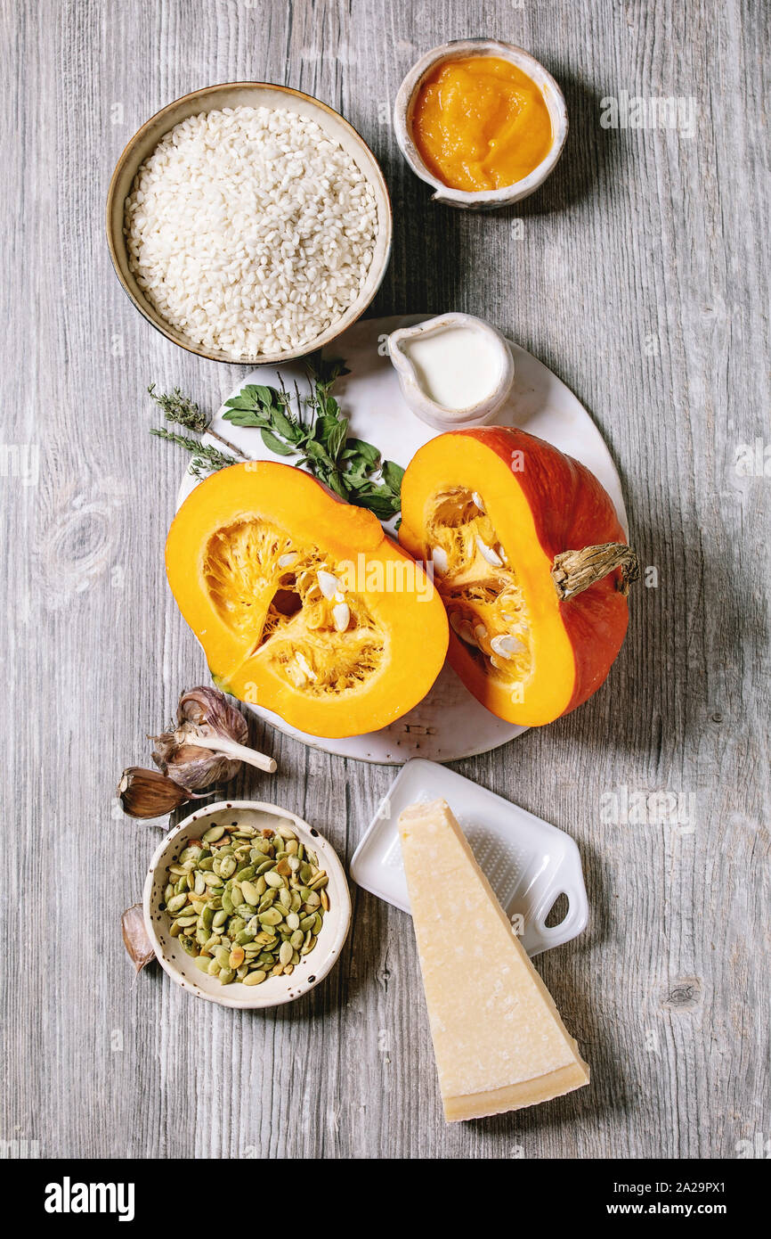 Gli ingredienti per cucinare il risotto di zucca. Materie non cotti riso per risotti in vaso di ceramica, fette di zucca, crema, semi, parmigiano grattugiato, aglio ed erbe aromatiche ov Foto Stock