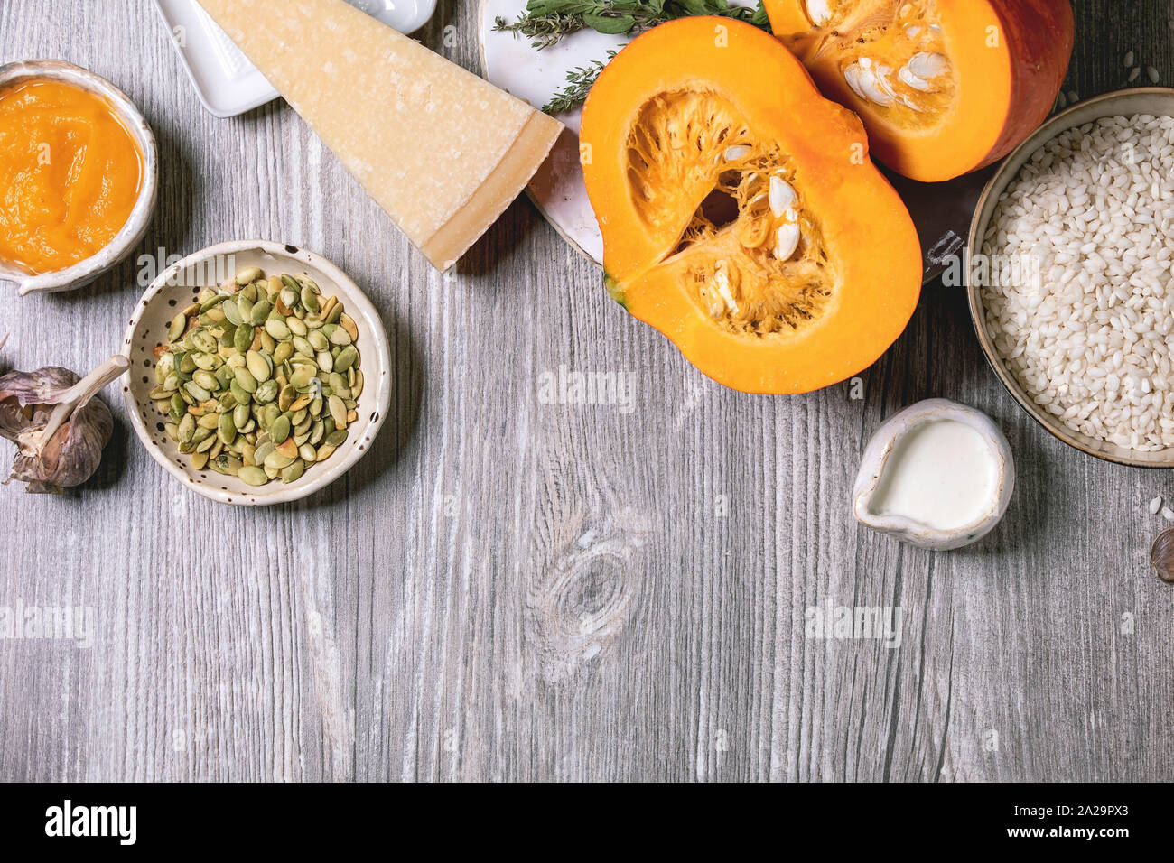 Gli ingredienti per cucinare il risotto di zucca. Materie non cotti riso per risotti in vaso di ceramica, fette di zucca, crema, semi, parmigiano grattugiato, aglio ed erbe aromatiche ov Foto Stock