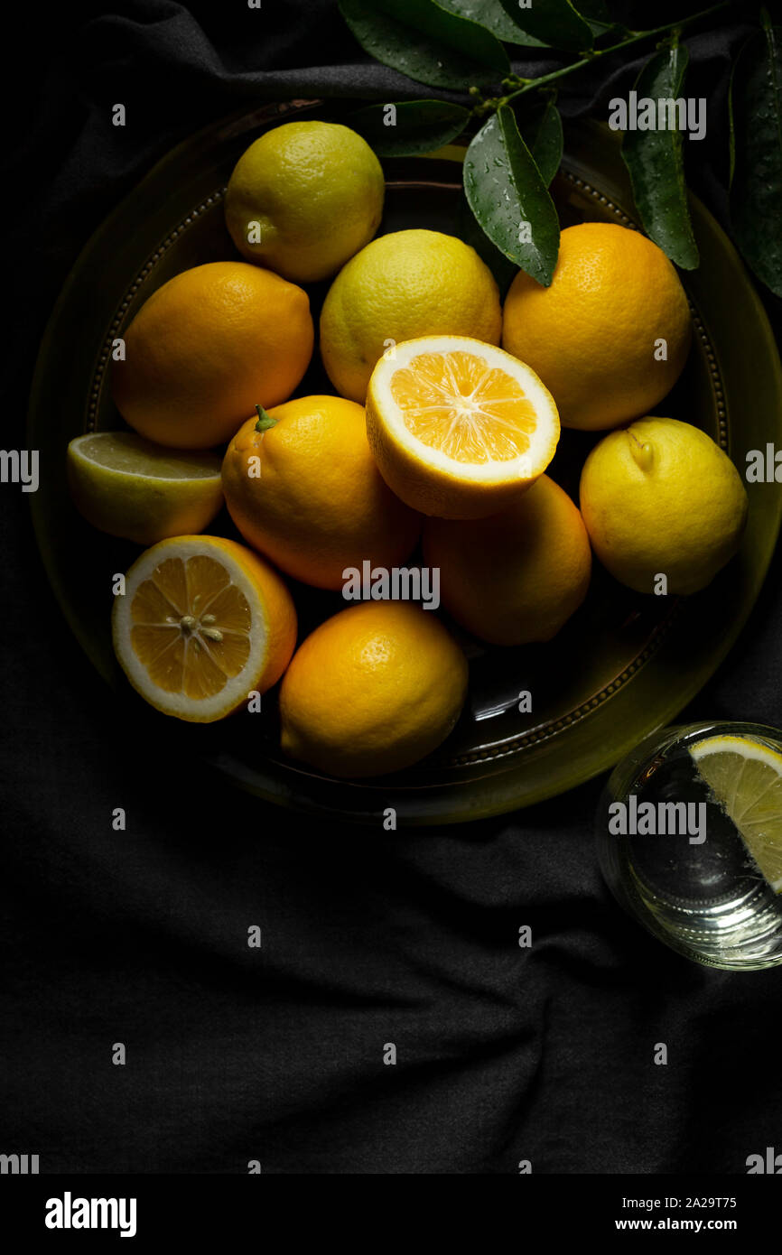 Un verde oliva piatto della casa dei limoni coltivati su un grigio scuro tovaglie di lino, con un bicchiere d'acqua. Foto Stock
