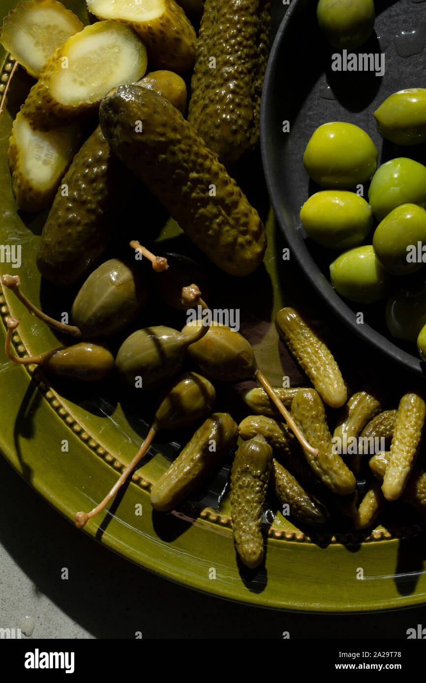 Una selezione di cetriolini sottaceto, bacche di capperi e olive verdi su un verde oliva piastra. Foto Stock