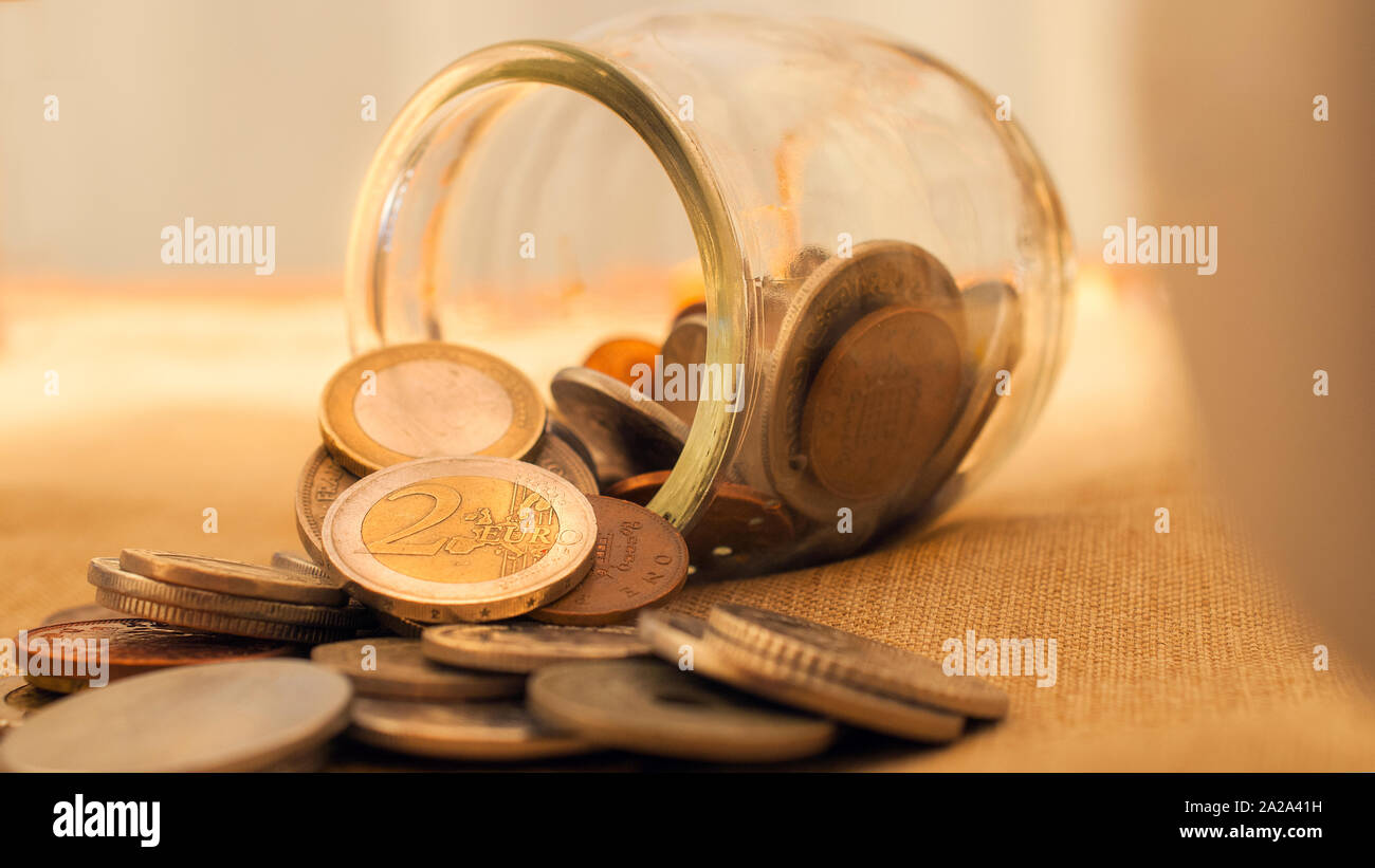 Coin jar capovolta sul tavolo con le monete in euro. Questa immagine può essere utilizzata per rappresentare diversi concetti relativi al denaro. Foto Stock