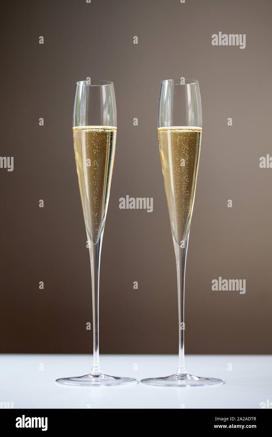 Due flauti champagne contenente vino bianco frizzante su una barra bianca top Foto Stock