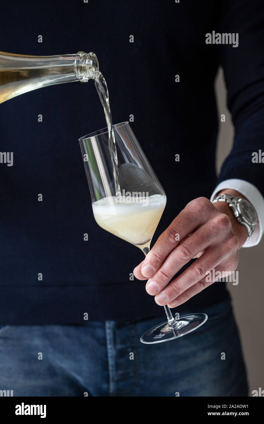 Un uomo che indossa un top scuro e jeans versa vino spumante in un bicchiere Foto Stock