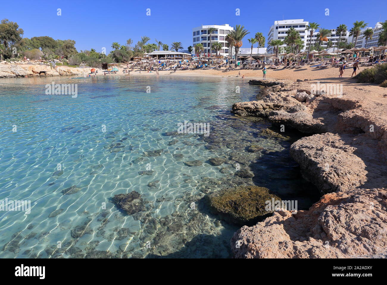 Bella Baia / laggon con clear cristal mediterraneo di acqua di mare, rocciosa e sabbiosa spiaggia di Agia Napa, Cipro, palme e hotel edifici contro il blu . Foto Stock