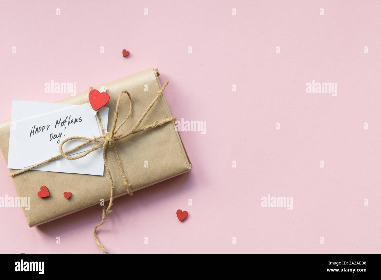 Presente avvolto in marrone carta craft e barra di filo di canapa su luce sfondo rosa. Confezione regalo con auguri per la festa della mamma. Vista dall'alto. Foto Stock