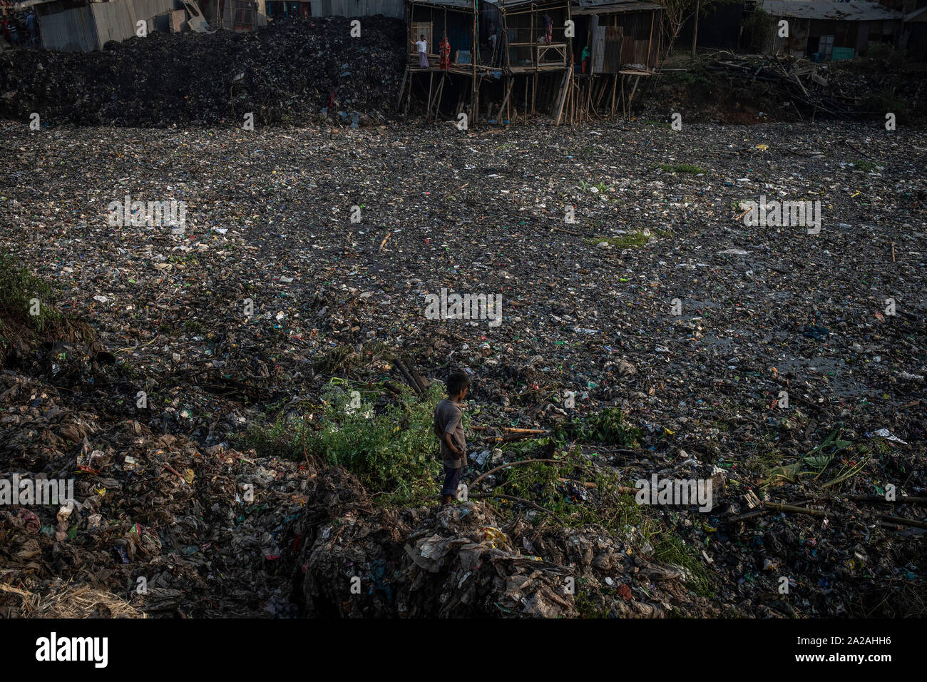 Un ragazzo si erge sul bordo della fortemente inquinato fiume Buriganga nella capitale Dhaka, Bangladesh, 26 aprile 2019. Foto Stock