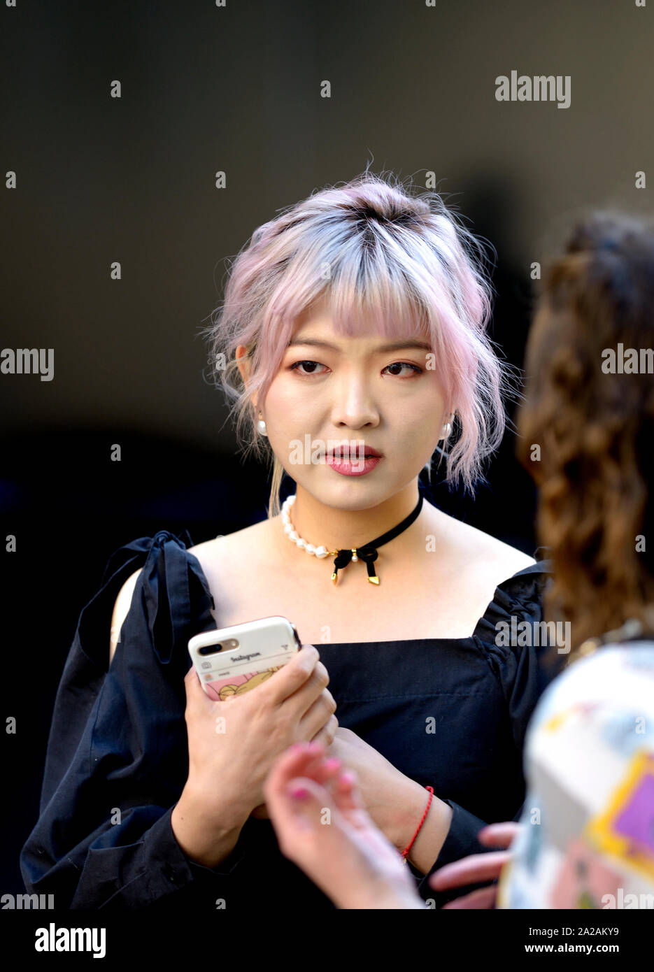 Giovane donna giapponese con telefono cellulare e capelli rosa presso la London Fashion Week, 2019. Foto Stock