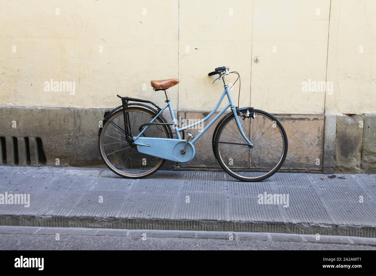 Adorabile immagine isolata di un blu vintage in bicicletta sulla strada dell'Italia, con un retrò marrone sedile in pelle. Appoggiata contro una parete. Foto Stock