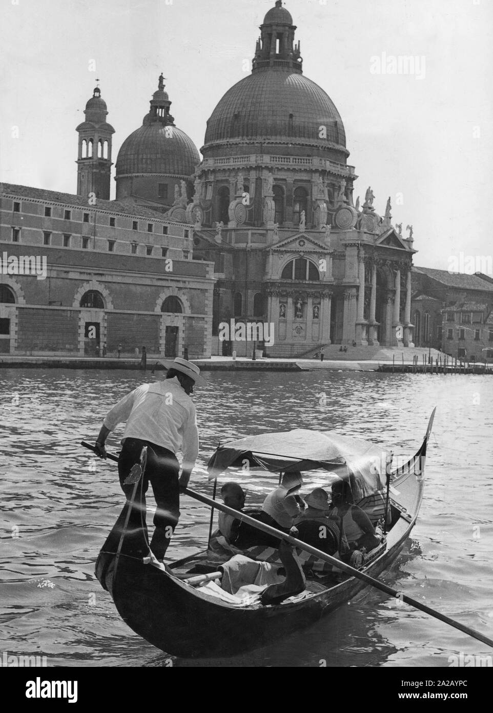 Un gondoliere porta i turisti attraverso il Canal Grande. Sulla riva della Basilica di Santa Maria della Salute può essere visto. Foto Stock