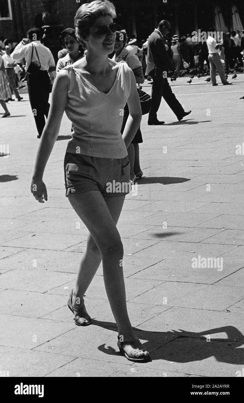 Un turista tedesco in una zona pedonale di una città italiana sul mare Adriatico presenta il look casual della fine degli anni cinquanta: top senza maniche, stretto shorts e sandali. Foto Stock