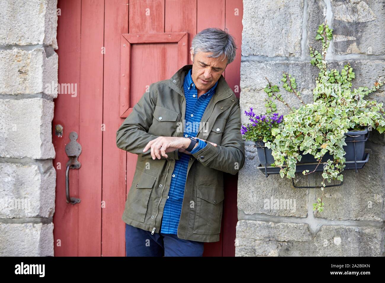 Uomo maturo guardando il suo orologio, in attesa. Rue Pocalette, architettura basca, Ciboure, Aquitaine, Paese Basco, Francia Foto Stock
