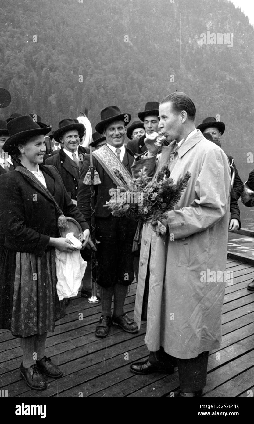 Il federale allora Ministro degli Interni Gerhard Schroeder (CDU) riceve un mazzo di fiori da un gruppo di musicisti in costumi tradizionali durante il Almer pellegrinaggio a San Bartolomeo del Koenigssee. Sullo sfondo il Koenigssee. Foto Stock