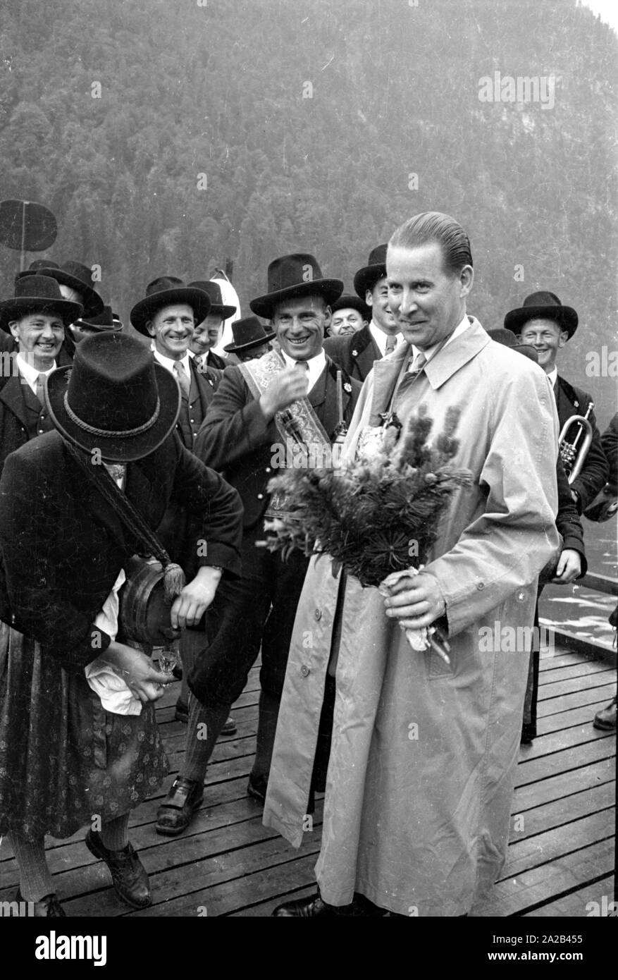 Il federale allora Ministro degli Interni Gerhard Schroeder (CDU) riceve un mazzo di fiori da un gruppo di musicisti in costumi tradizionali durante il Almer pellegrinaggio a San Bartolomeo del Koenigssee. Sullo sfondo il Koenigssee. Foto Stock