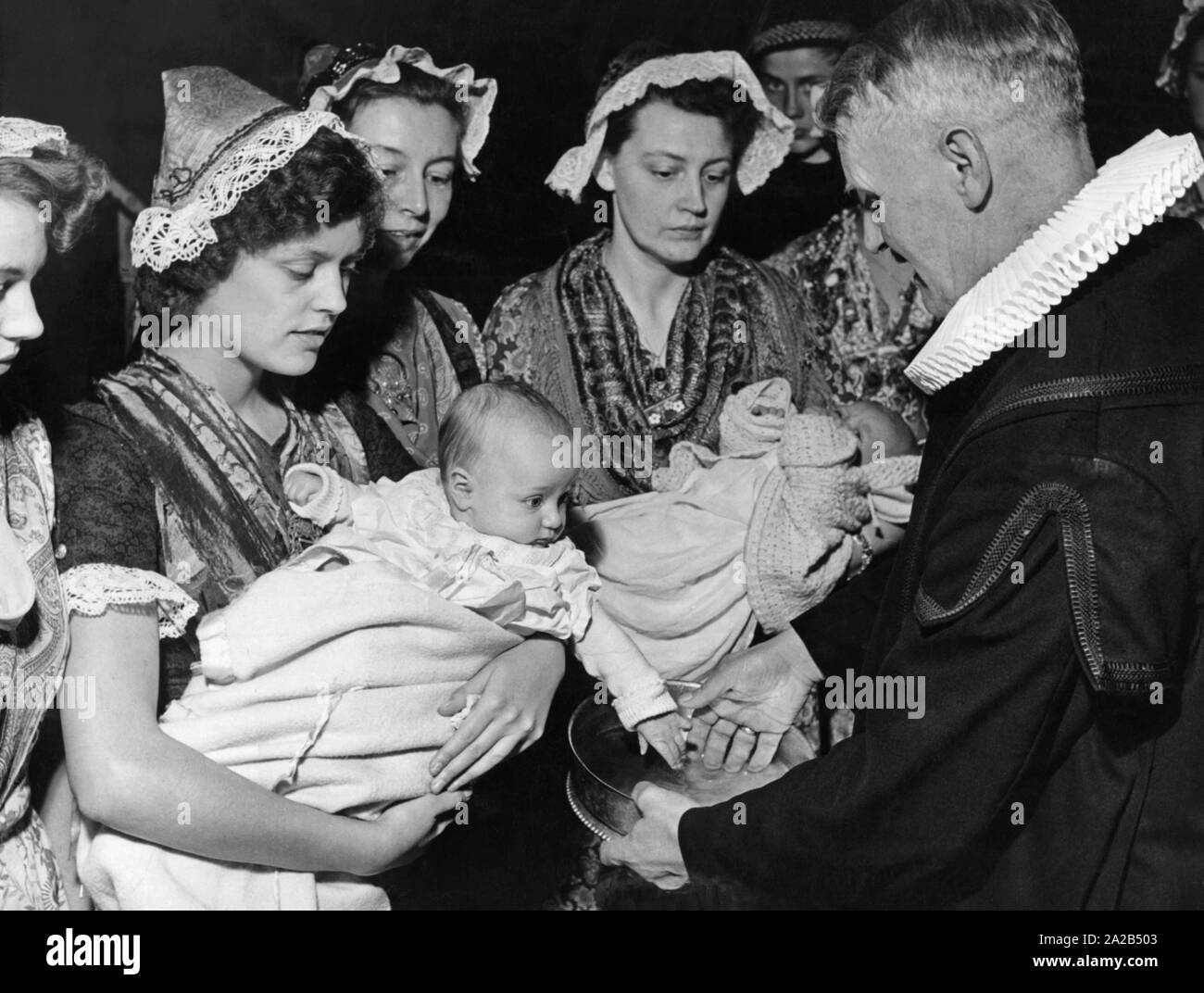 Due bambini sono battezzati da un pastore protestante. Essi vengono trattenuti dalle loro madri che indossano costumi tradizionali. Questa foto è stata presumibilmente preso poco dopo il ripopolamento dell'isola. Foto Stock
