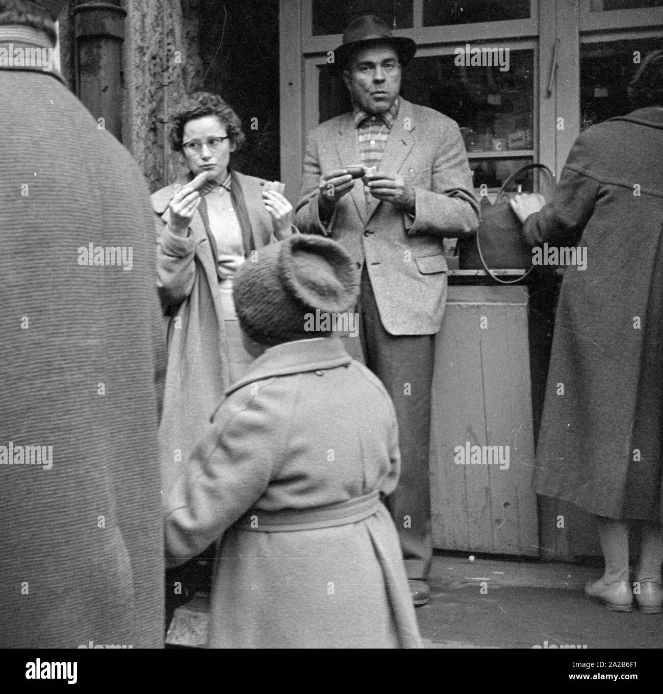 Scena di strada in Leipzig durante la Fiera di primavera 1960. Due persone con il Bratwurst (salsicce fritte). Foto Stock